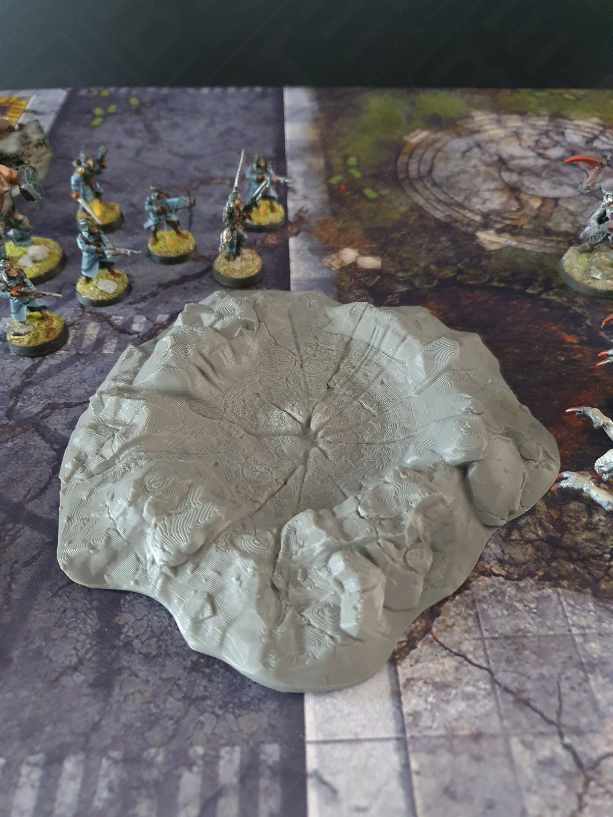 Grey 3D printed crater terrain with intricate textures on a battle mat, enhancing sci-fi wargaming scenes.