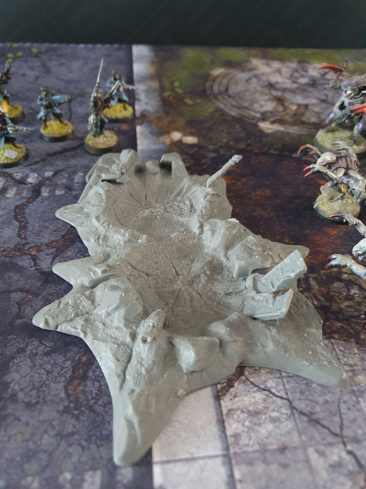3D printed grey crater scatter terrain for sci-fi wargaming, with miniature figures on a battle mat for scale.