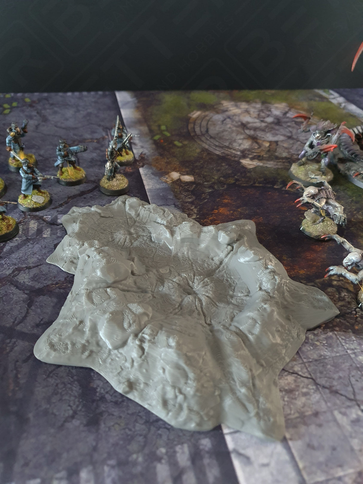 Grey 3D printed crater scatter terrain with miniature figures on a wargaming mat, enhancing sci-fi tabletop scenery.